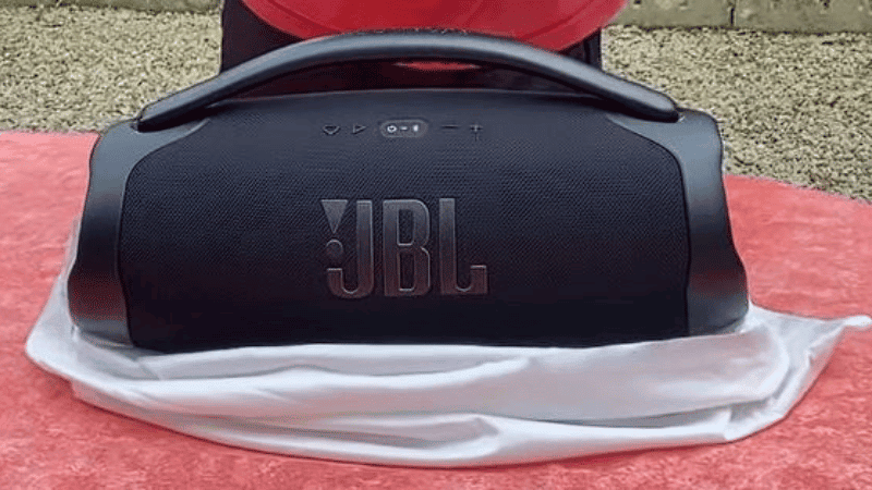 Vue au premier plan de l'enceinte portable JBL Boombox 3 Wi-Fi allumée et posée sur une table, avec notre testeur au second plan.